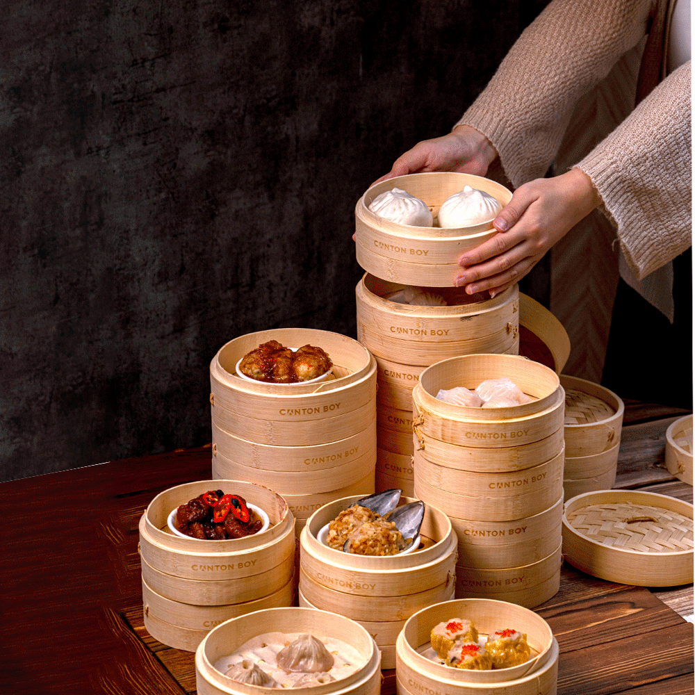 A chef stacking dim sum baskets which include dishes like bbq chicken pao, crystal har gow, siu mai king, chicken xiao long bao, and more